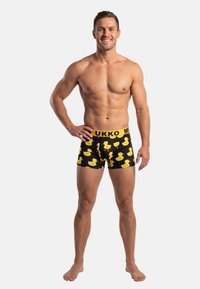 Zwarte boxershorts met een patroon van gele rubberen eendjes. Elastische tailleband met "UKKO"-branding in het geel. Gladde stoftextuur.