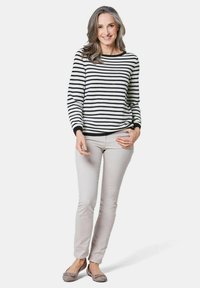 Schwarz-weiß gestreifter Pullover, lange Ärmel, lockere Passform; hellbeige, schmal geschnittene Hose; graue Ballerinas mit Schleifendetail; neutraler Hintergrund.