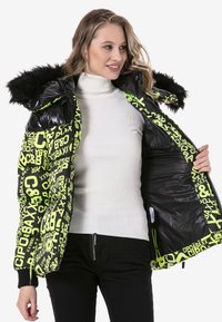 Donsjack met een glanzend zwart exterieur en neon groene logoprint. Beschikt over een met nepbont gevoerde capuchon en een zwarte binnenvoering.
