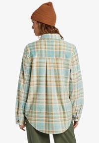 Flannel shirt in light blue, beige, and orange plaid. Features a curved hem, button cuffs, and a soft, textured fabric.