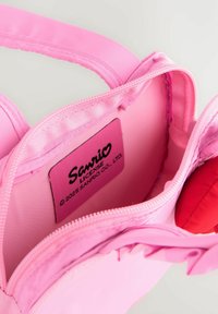 Intérieur d'un sac zippé rose montrant l'étiquette de licence Sanrio et une partie d'un nœud rouge attaché au sac.