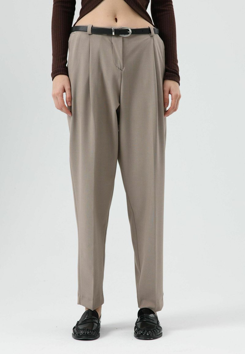Pantalon beige sur mesure avec une taille haute, des plis à l'avant et une ceinture noire. Le tissu semble lisse ; ajusté à la taille et ample au niveau des jambes.