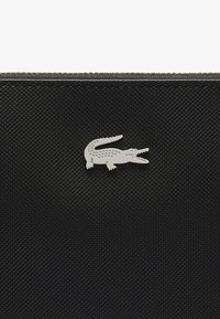 Pouch nero testurizzato con logo in argento a forma di coccodrillo. La superficie presenta un motivo a diamante unico, creando un aspetto strutturato.