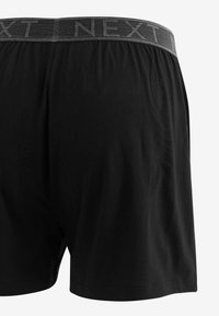 Schwarze Boxershorts aus weichem Stoff mit einem elastischen Bund, der mit grau gestreiftem Text "NEXT" bedruckt ist. Einfaches, glattes Design.