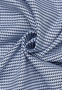 Tessuto a scacchi blu e bianco caratterizzato da una trama testurizzata con un motivo geometrico, che mostra morbidezza e una caduta moderata.