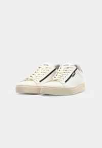 B baskets en cuir blanc avec une semelle texturée, une bande noire sur le côté et un logo de marque sur la languette. Doublure intérieure en gris doux.
