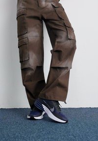 Barna cargo nadrág több zsebbel, puha textúrával és laza szabással, sötétkék Nike cipővel, fehér részletekkel párosítva.
