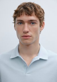 Light blue polo shirt made of soft fabric with a three-button placket and a classic collar, featuring a slim fit and minimal design.