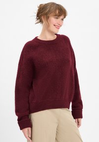 Burgundy knit sweater with a relaxed fit, round neckline, and ribbed cuffs. Soft, textured fabric with a slightly fuzzy appearance.