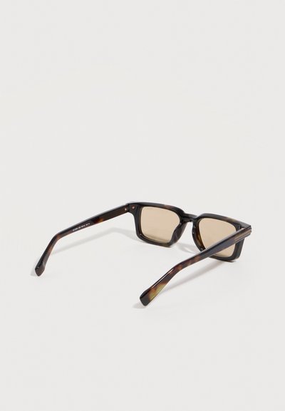 Ορθογώνια γυαλιά ηλίου με μοτίβο χελώνας και καφέ σκουρόχρωμους φακούς, εμφανιζόμενα από πίσω επάνω σε λευκή απλή επιφάνεια.