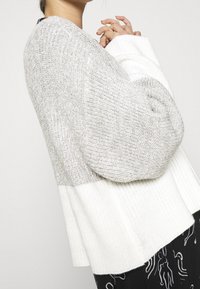 Maglione chunky lavorato a maglia con un design a blocchi di colore grigio e bianco, polsini a coste e una vestibilità rilassata con spacchi laterali per un maggiore comfort.