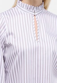 Blouse rayée en coton gris clair et blanc, dotée d'un col montant à volants, d'une ouverture clé à l'avant et d'une fermeture par bouton au niveau du cou.