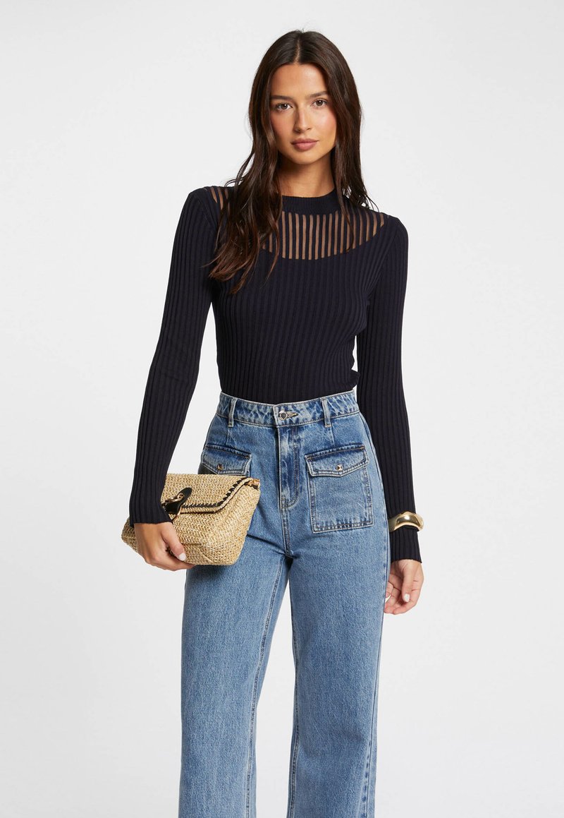 Haut noir à manches longues côtelé avec un col en dentelle rayé, associé à un jeans large taille haute en denim bleu et à un sac à main en osier beige.