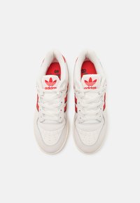 Biele atletické sneakers so svetločervenými akcentmi a tromi pruhmi, s textúrovaným koženým zvrškom, perforovanou špicou a polstrovaným golierom.