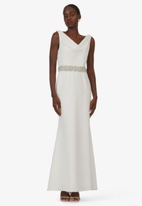 Langes weißes Kleid mit einem drapierten Cowl-Halsauschnitt, verziert mit einem silbernen Gürtel in der Taille und einem glatten, fließenden Stoff. Elegantes und minimalistisches Design.