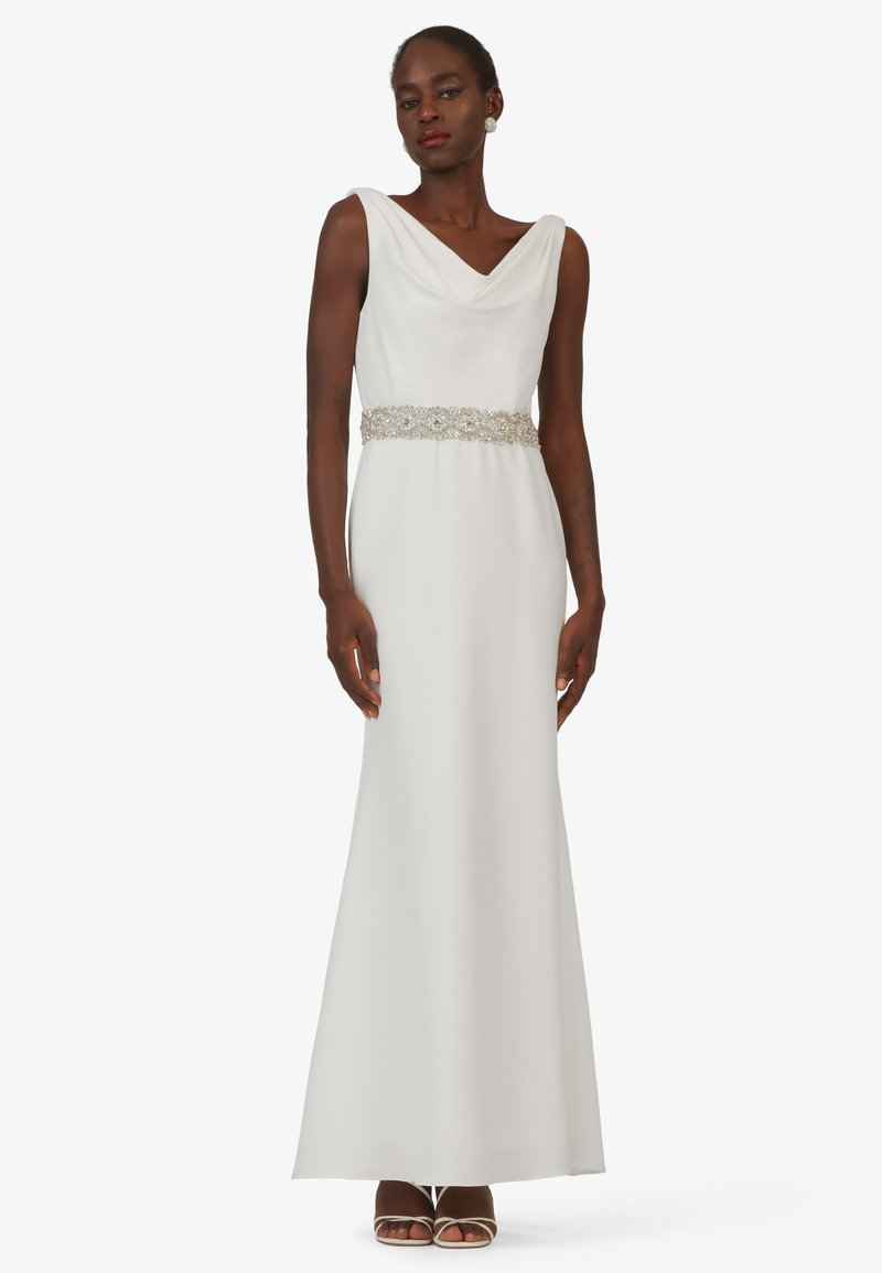 Langes weißes Kleid mit einem drapierten Cowl-Halsauschnitt, verziert mit einem silbernen Gürtel in der Taille und einem glatten, fließenden Stoff. Elegantes und minimalistisches Design.