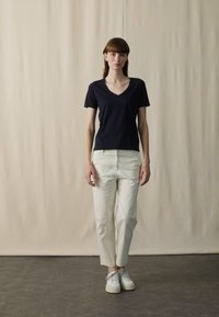 Tengerészkék V kivágott póló és krém színű, tapered nadrág, fehér sportcipővel párosítva. Természetes anyagú, minimalista kialakítású és laza szabású.