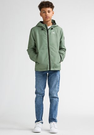 Grüne Kapuzenjacke mit Reißverschluss vorne, elastischen Bündchen und zwei Seitentaschen, kombiniert mit hellblauen Jeans und weißen Turnschuhen.