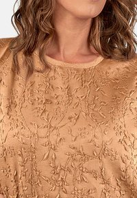 Beige tekstureret top med blomsterbroderi, rund udskæring og korte ærmer. Materialet har et blødt, let hævet mønster.