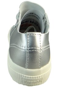 Srebrne, syntetyczne sneakersy z gładkim, metalicznym wykończeniem, białą gumową podeszwą i teksturowanym czubkiem; mają branding na pięcie.