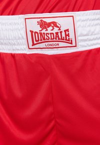 Crvene kratke hlače od glatkog materijala s bijelim elastičnim pojasom. Ima oznaku s logom tigra i tekstom "Lonsdale London."