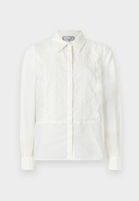 Λευκό μακρυμάνικο πουκάμισο με δαντελένιες εμπρόσθιες πλάκες, κυματιστά άκρα, κούμπωμα με κουμπιά και μυτερό γιακά, παρουσιασμένο σε απλό φόντο.