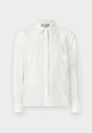 Blouse blanche à manches longues avec panneaux avant en dentelle, bords festonnés, fermeture à boutons et col pointu, présentée sur un fond uni.