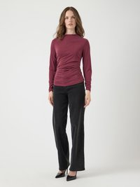 Bordeaux lang mouw top met geplooid detail bij de taille, gecombineerd met hoge zwarte jeans en zwarte puntige hakken.