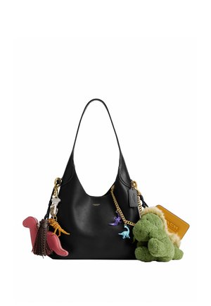Sac à bandoulière noir décoré de porte-clés dinosaures colorés, d'un dinosaure en peluche vert, d'une chaîne dorée et d'une étiquette en cuir Coach.