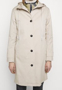 Beige lichtgewicht jas met capuchon, voorzien van een knoopsluiting aan de voorkant, twee zijzakken en trekkoordaccenten op de capuchon en manchetten.