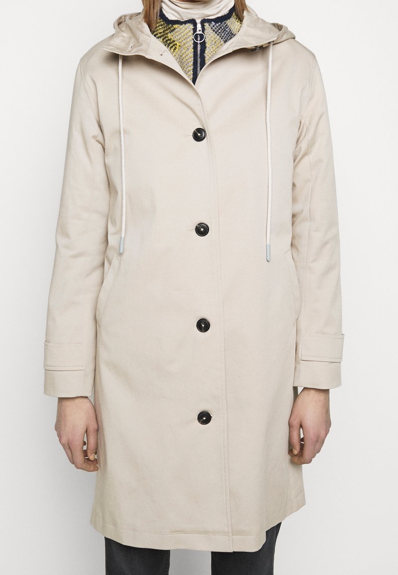 Beige lichtgewicht jas met capuchon, voorzien van een knoopsluiting aan de voorkant, twee zijzakken en trekkoordaccenten op de capuchon en manchetten.