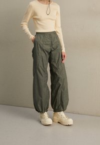 Top lungo a maniche ribbed color beige chiaro abbinato a pantaloni larghi verde oliva e stivaletti chunky beige con suole rigate.