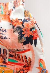 Tessuto colorato con motivi floreali in arancione e blu navy, con sfondo crema. Include illustrazioni di una scena a bordo piscina e di edifici.