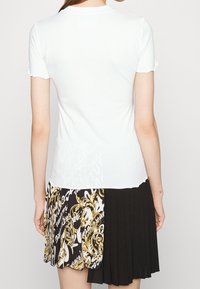 Vit kortärmad T-shirt med rund halsringning, med en mjuk textur. Matchad med en mönstrad svart och vit plisserad kjol.