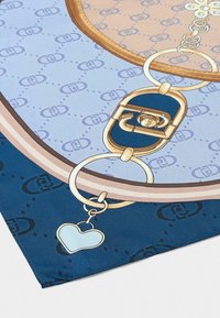 Foulard in seta con un motivo decorativo in blu e beige, dotato di un elegante fermaglio dorato e di un piccolo ciondolo a forma di cuore.