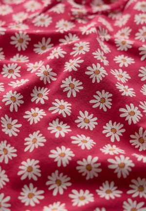 Rode stof met een herhalend patroon van witte madeliefjes met gele kern, met lichte plooien en textuur.