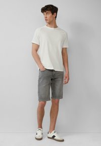 Witte t-shirt met korte mouwen, grijze denim shorts en witte sneakers met zwarte accenten. De shorts zijn kniehoog met een standaard pasvorm.
