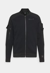 Černá bomber bunda se zipem vpředu, žebrovanými manžetami a lemem, postranními kapsami a detaily na ramenou. Vyrobena z hladké látky s matným povrchem.