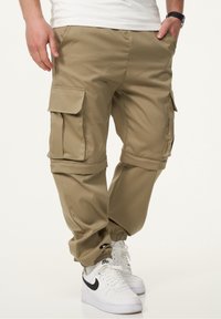 Beige Cargo-Hosen mit elastischen Bündchen, mehreren Seitentaschen und einem strapazierfähigen Stoff. Kombiniert mit weißen Nike Sneakers.