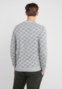 Sweatshirt grigio con un motivo circolare nero, colletto e polsini a coste, e vestibilità rilassata. Abbinato a pantaloni verdi scuri.