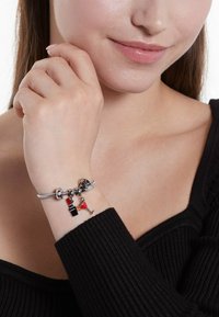 Zilveren armband met bedels in de vorm van een cocktail en een rode jurk, met een gestructureerde zilveren band, gedragen op een hand met een lichte huidskleur.