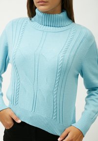 Helles blaues gestricktes Sweatshirt mit hohem Rippkragen, das über Zopfmuster und gerippte Säume verfügt. Weiche Textur und taillierte Passform.