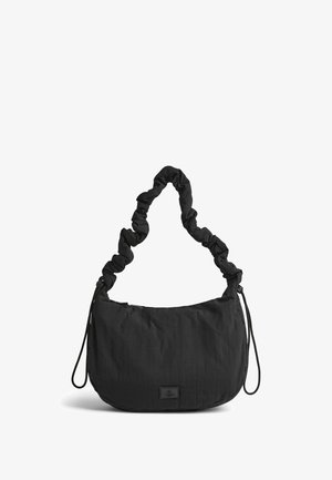 Sort stof håndtaske med en samlet rem, blød tekstur, rund form, lynlåslukning og et lille logo-patch på fronten.