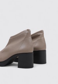Beige Leder Stiefeletten mit runder Zehenpartie und strukturiertem schwarzen Blockabsatz. Mit gesteppten Details entlang der oberen Kante.