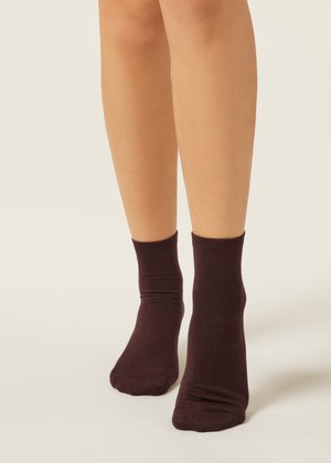 Nohy obuté v tmavě hnědých ponožkách po kotníky na světlém pozadí, zobrazující přední a boční pohled na nohy.