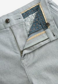Pantalons gris clair avec un tissage texturé, dotés d'une doublure intérieure à motif bleu contrastant et d'une fermeture éclair avec un bouton.