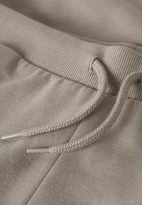 Ljusbeige mjukisbyxor med ribbad midjeresår och flätad dragsko. Mjuk tygstruktur med metallspetsar på dragskon.