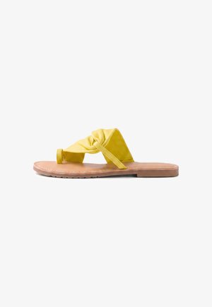 Sandalia amarilla tipo slip-on con nudo, suela plana color cuero, tira ancha de tela y puntera abierta, mostrada de perfil sobre fondo blanco.