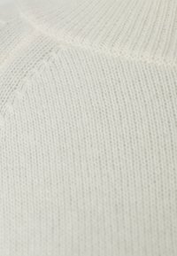 Tissu en tricot crème clair avec une texture lisse et un motif côtelé. Présente un détail de couture subtil, créant une apparence douce et confortable.
