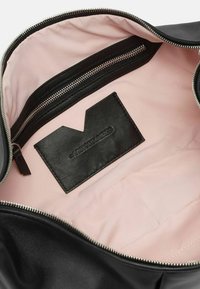 Interno di una borsa in pelle nera con una fodera rosa, dotata di un vano con zip e di un'etichetta in pelle nera con la scritta "VISIONAIRES" in rilievo.